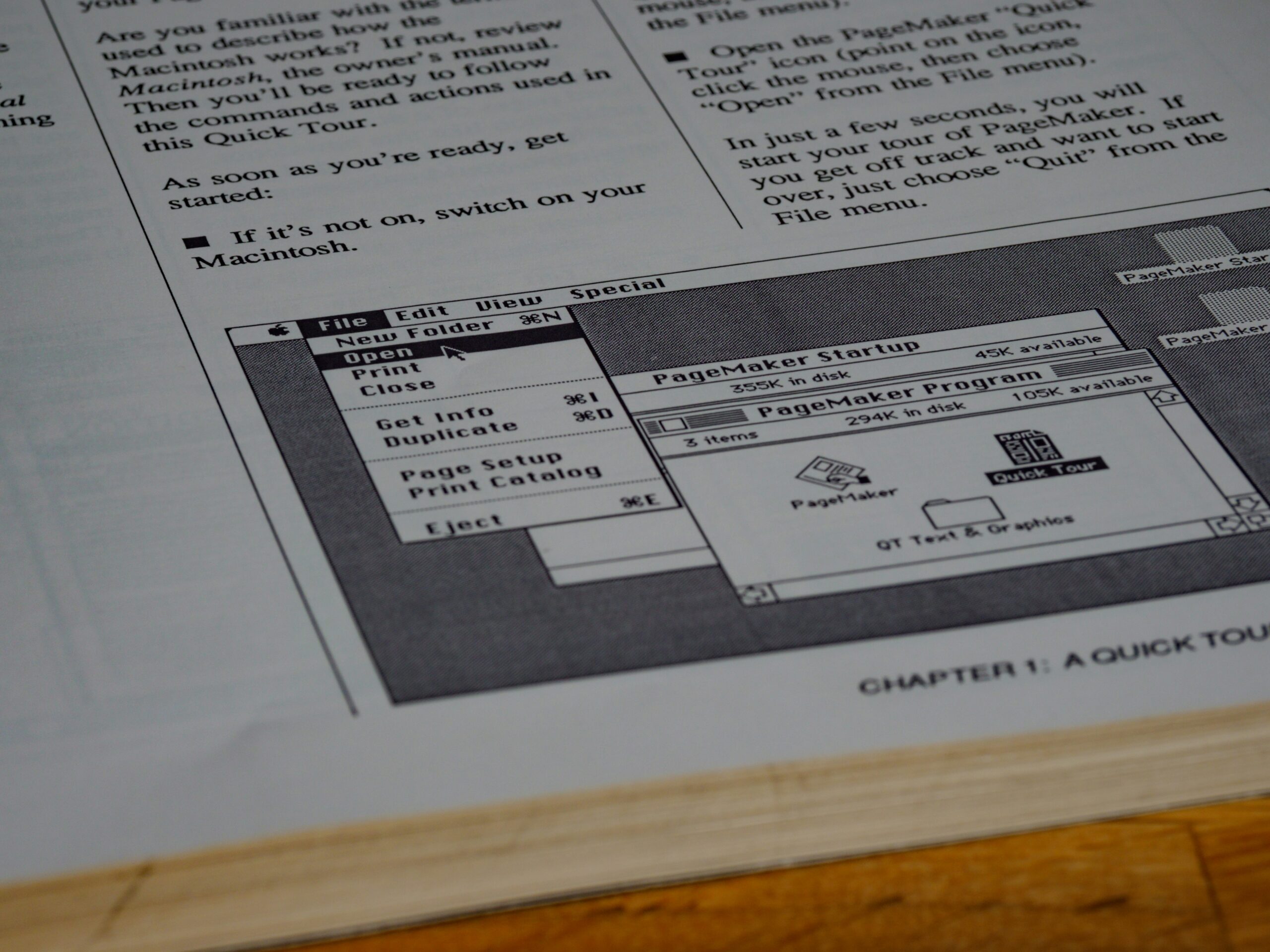 A photo by Brett Jordan of a screenshot of an old Macintosh computer interface showing a PageMaker software manual page. The image includes a menu bar with File, Edit, and View options, and shows instructions for a 'Quick Tour' of the software. The interface is characteristically black and white with the classic Mac OS design.