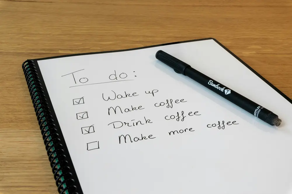 Handwritten to-do list and pen, sitting on a wooden desk.